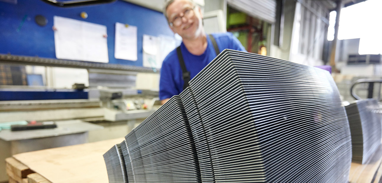 Stapel mit bearbeitetem Blech und lächelndem Mitarbeiter im Hintergrund